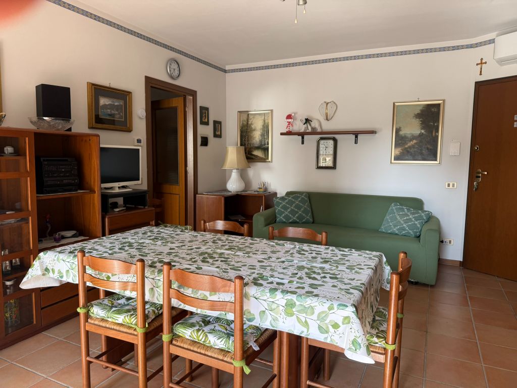 Soggiorno con tavolo da pranzo per quattro, divano letto verde e TV – Sirmione Bliss